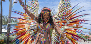 a woman in a colourful carnival costume on Kadooment Day in summer in Barbados. She is smiling and looking down with one hand in the air.