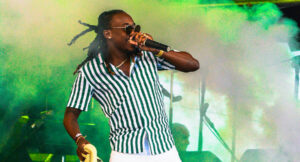 Singer 'Mole' performing on stage in Barbados wearing a striped button up shirt with green fog in the background
