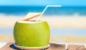 a green coconut with it's top cut off. it has a white straw in it.